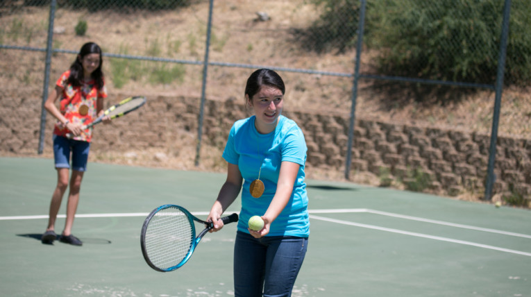 Teen girls with ball and raquets playing tennis on court