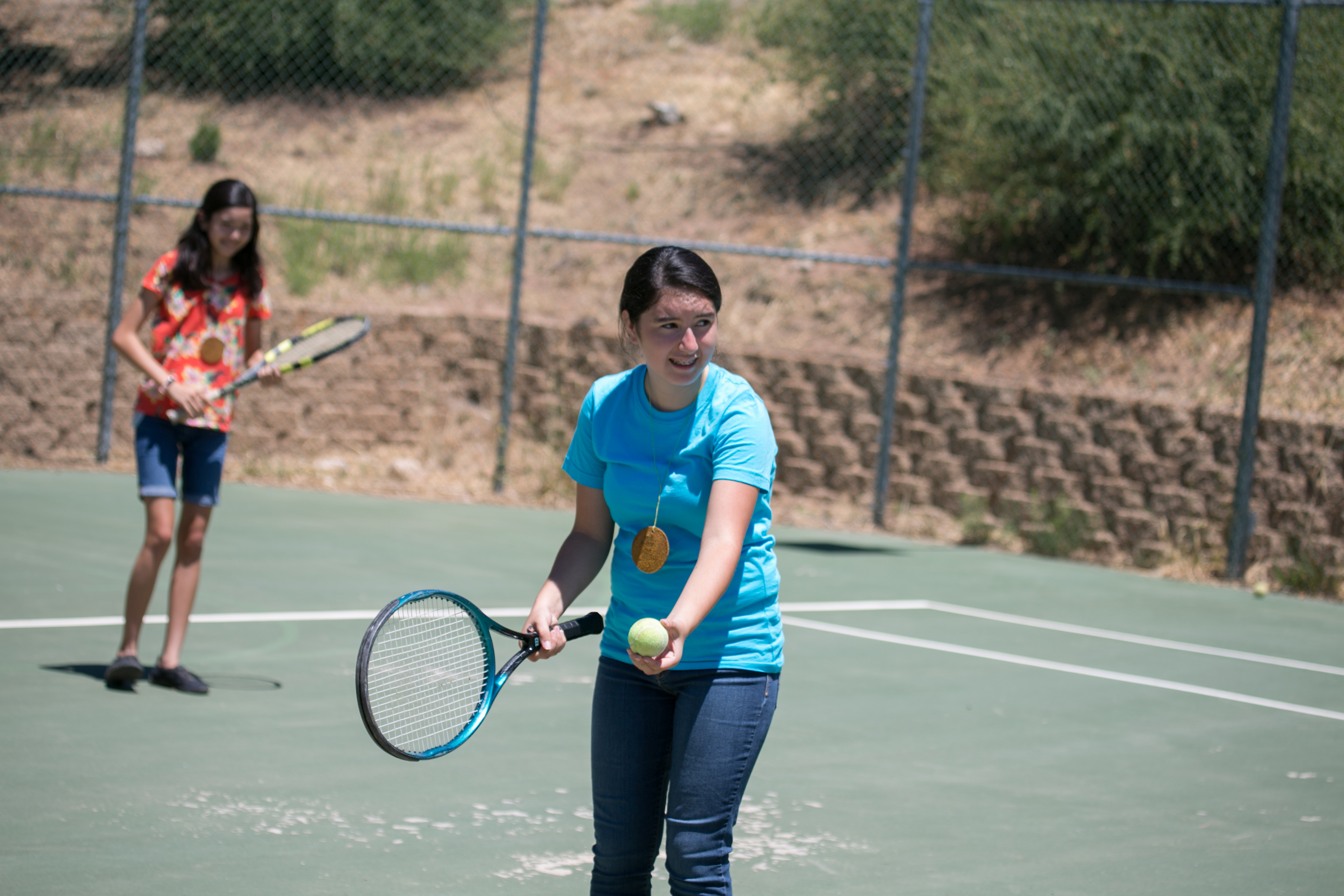 Teen girls with ball and raquets playing tennis on court