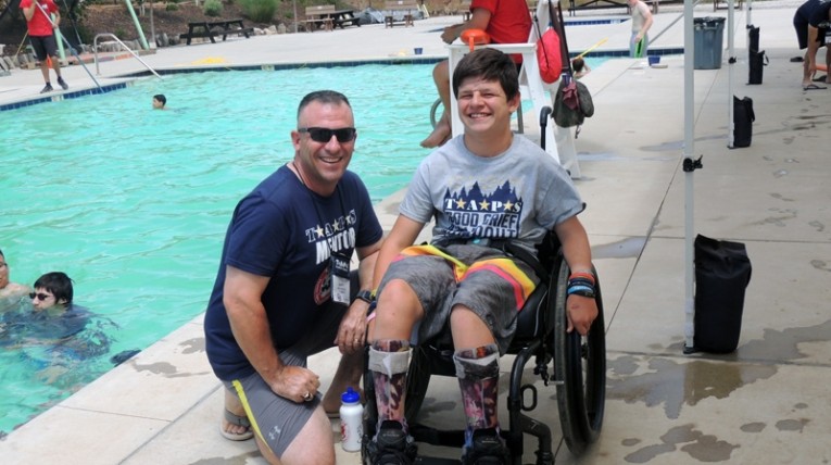 TAPS volunteer with boy in wheelchair on pool deck