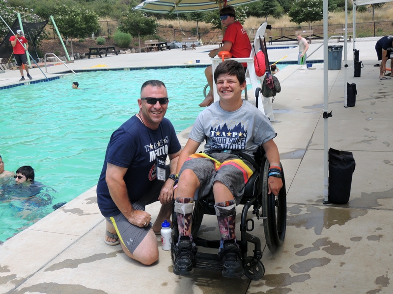 TAPS volunteer with boy in wheelchair on pool deck