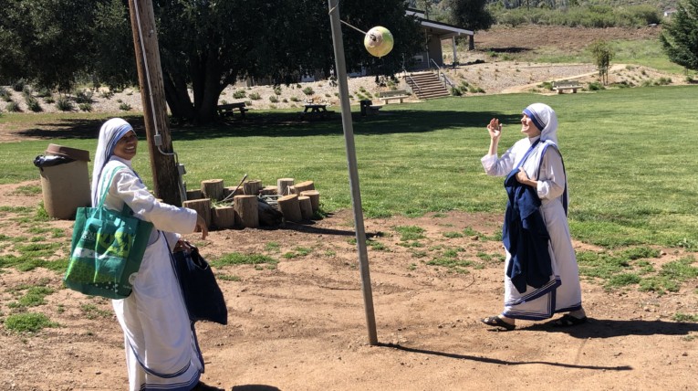 Two nuns in habits playing tetherball near meadow