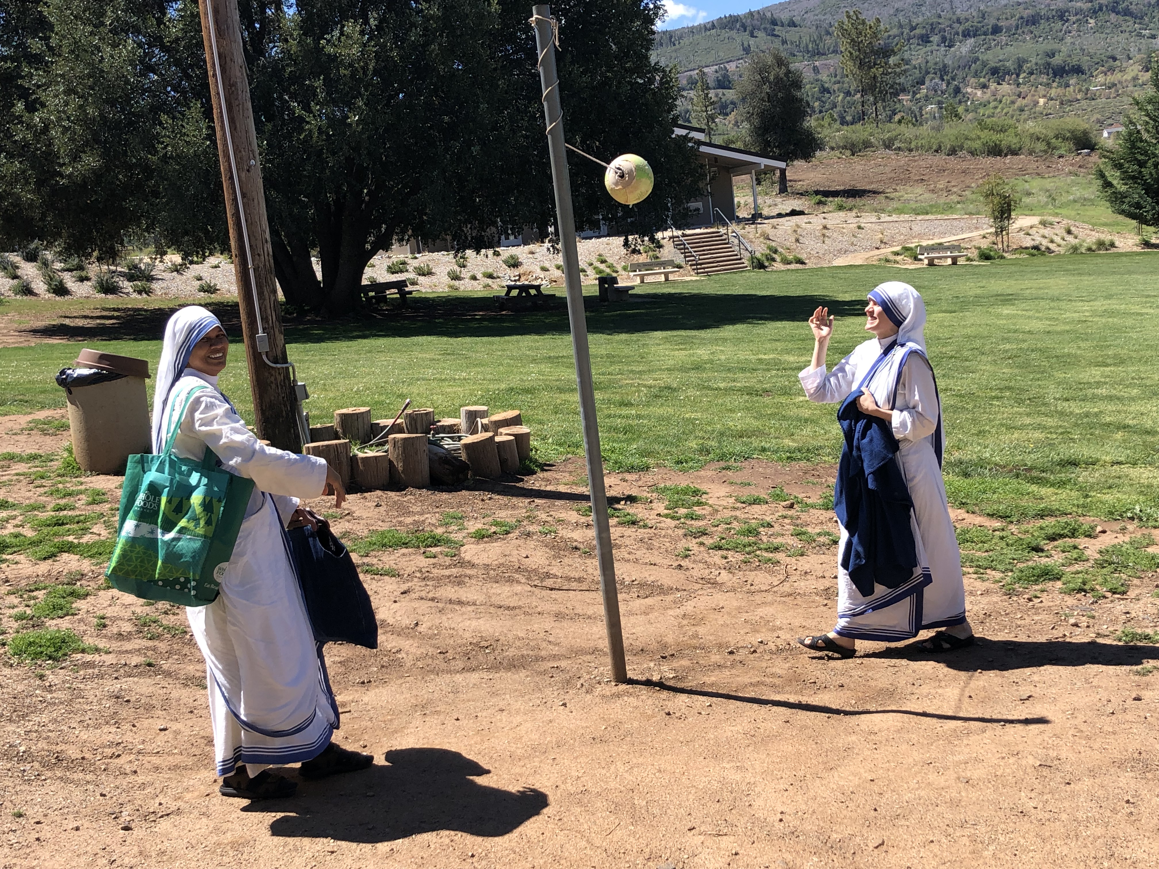 Two nuns in habits playing tetherball near meadow