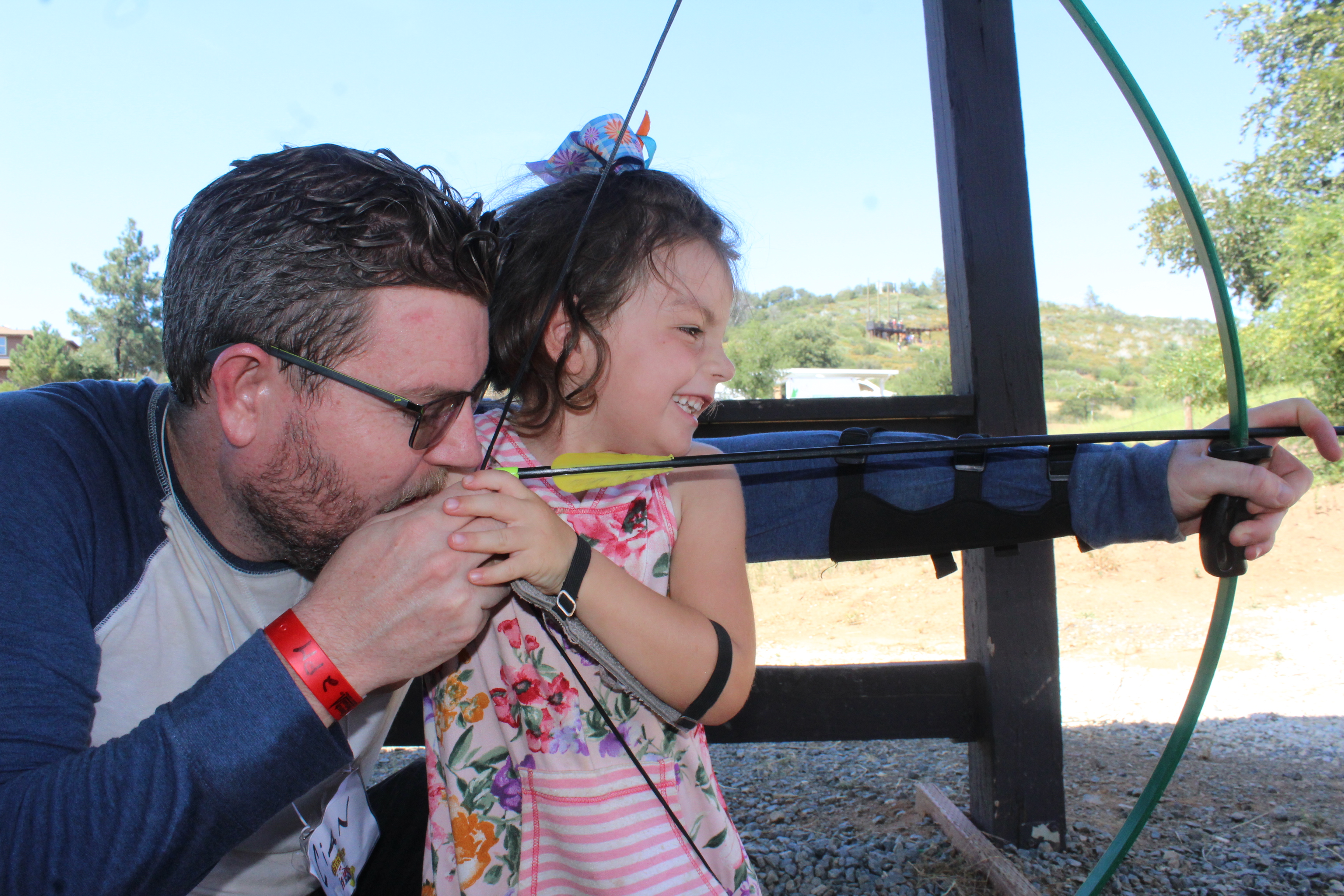 Dad helping girl aim bow and arrow during archery
