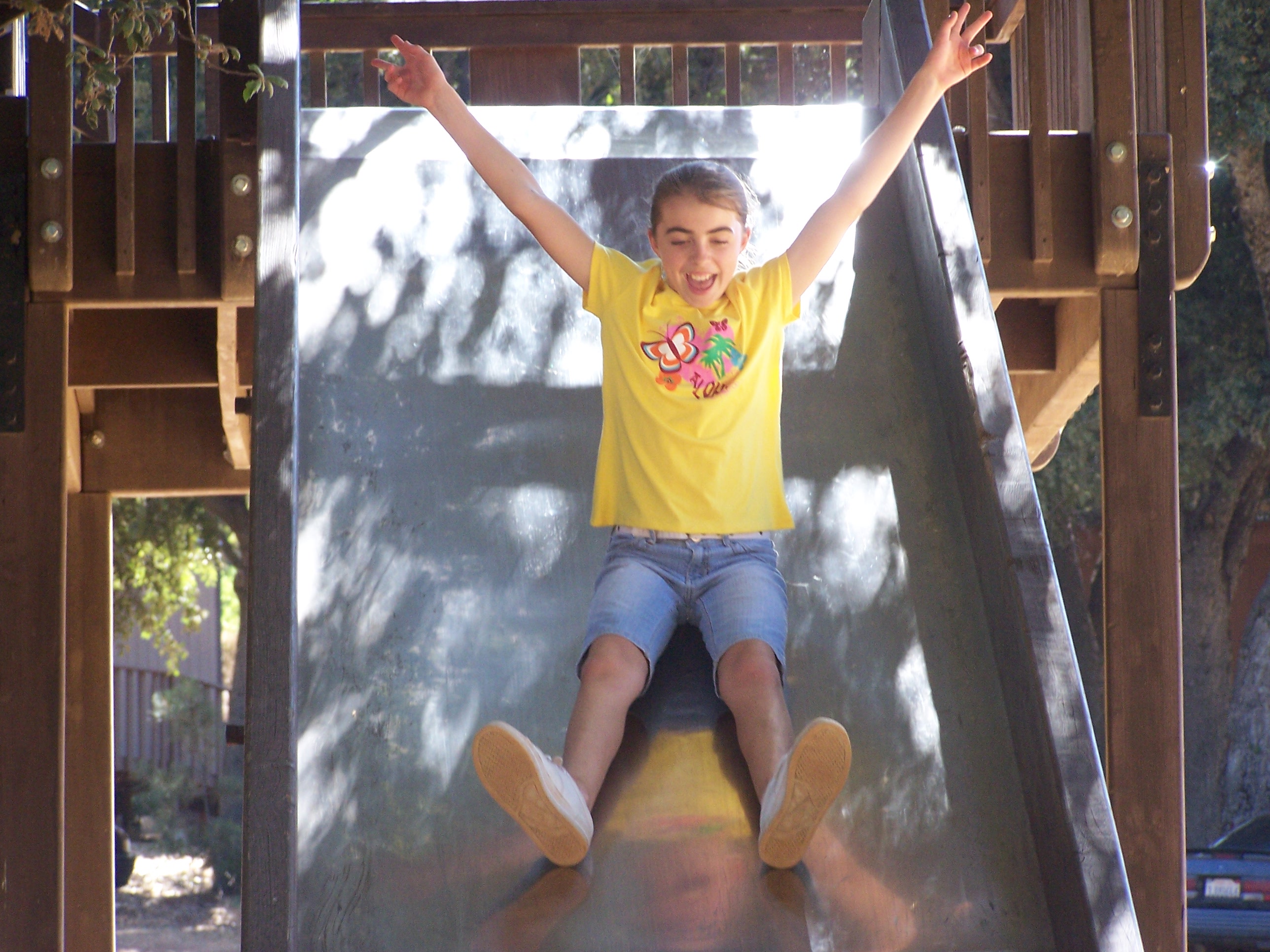 Girl sliding down treehouse slide with arms in the air
