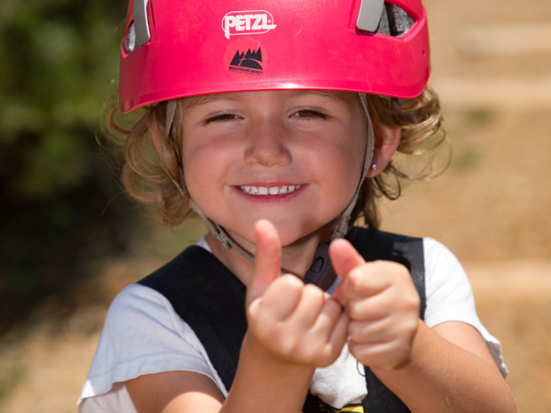 Young girl in helmet giving thumbs up sign after zipline ride