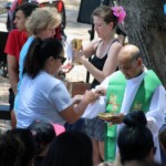 Adults receiving communion with priest during mass outdoors